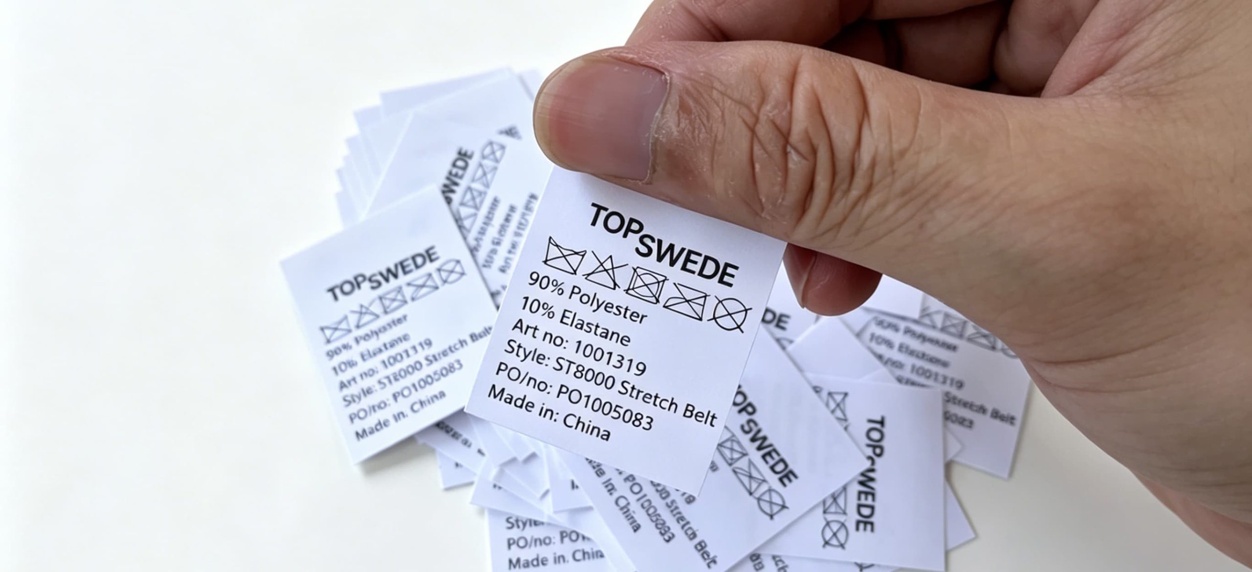 16:9 Banner | Macro close-up of eco printed polyester garment tags with full brand & specification info